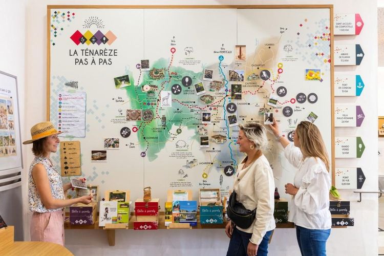 Des touristes devant le panneau du circuit de découvertes en Ténarèze à La Fabrique à souvenirs à l'Office de Tourisme à Montréal-du-Gers